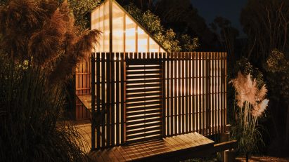 Mono-pitched polycarbonate shed on a wooden deck shining light through timber slats on a slope in the New Zealand bush