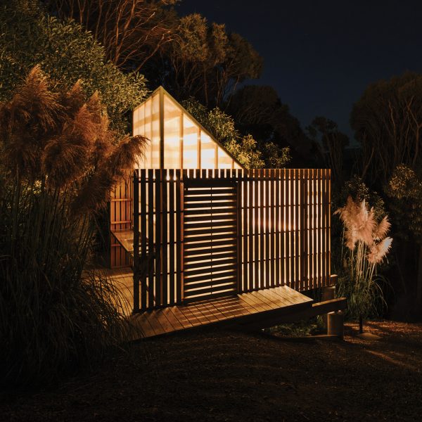 Mono-pitched polycarbonate shed on a wooden deck shining light through timber slats on a slope in the New Zealand bush