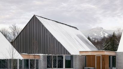 A series of pitched-roof structures with granite stone walls and metal-clad gable ends on a snowy mountainside