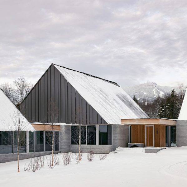 A series of pitched-roof structures with granite stone walls and metal-clad gable ends on a snowy mountainside