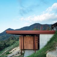 One-storey building with a red steel frame and concrete and wood walls extending out of a hillside