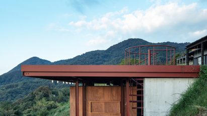 One-storey building with a red steel frame and concrete and wood walls extending out of a hillside