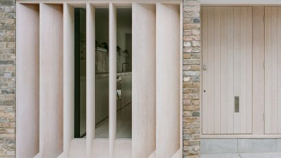 Exterior of a brick mews house with a timber door, timber louvres in front of a large window and a grey cat