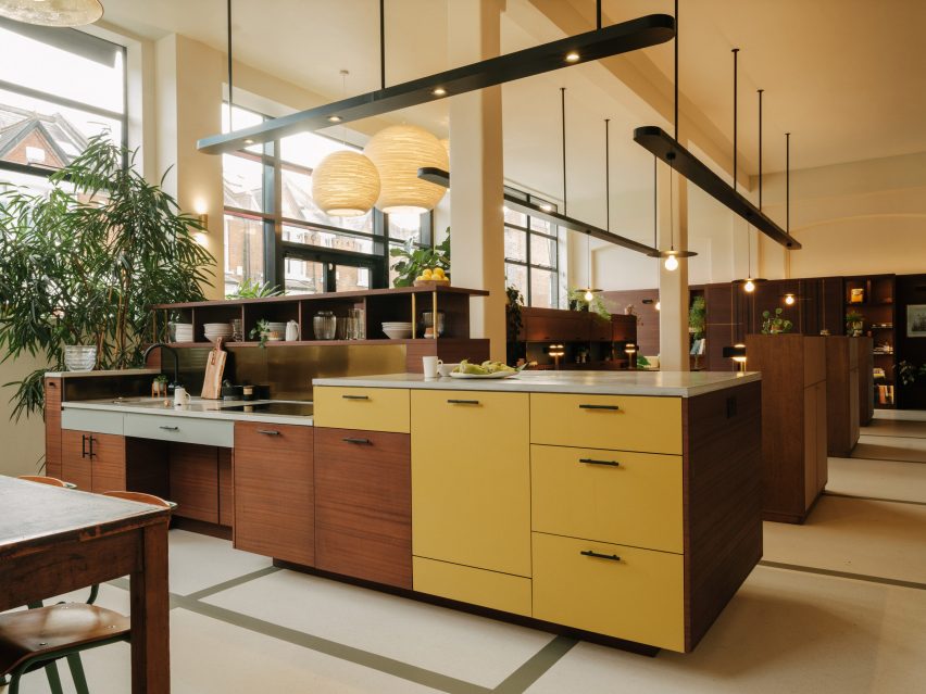 Kitchen island with wood and yellow-painted cupboard doors in an open-plan office with overhead pendant lamps
