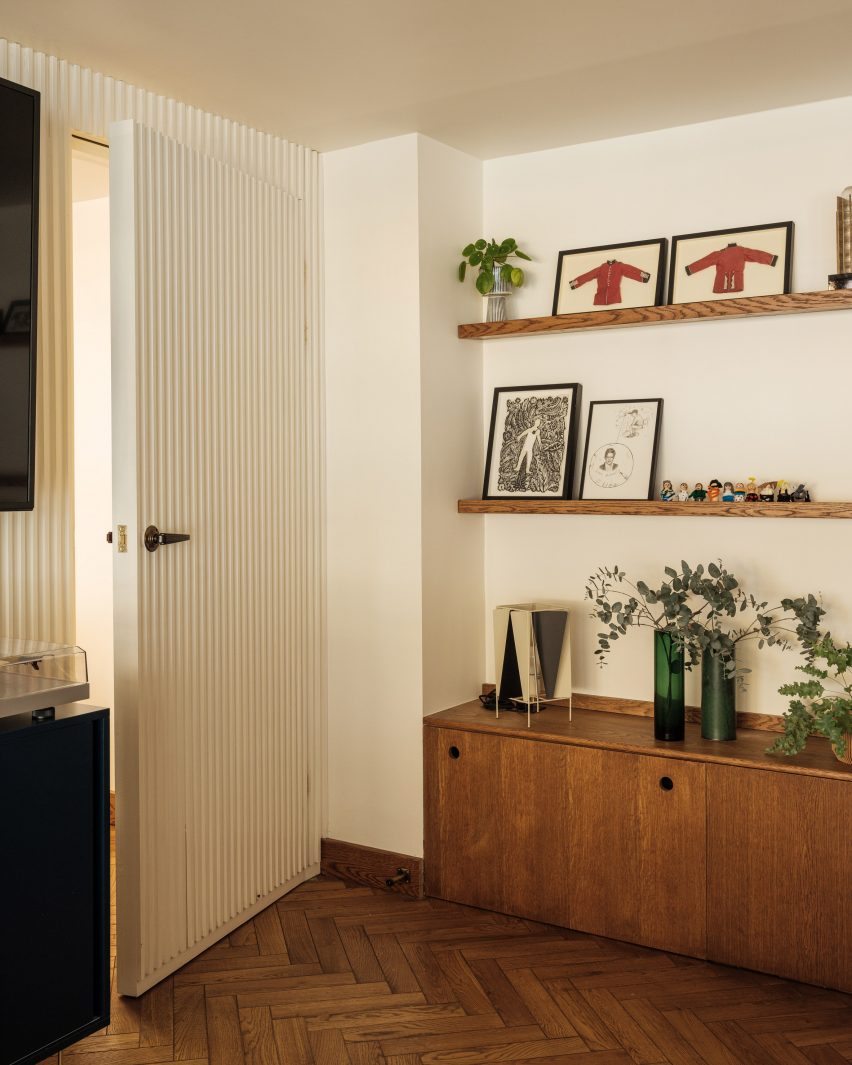 Corner of a room with white walls, parquet flooring, wood side cabinet and shelving