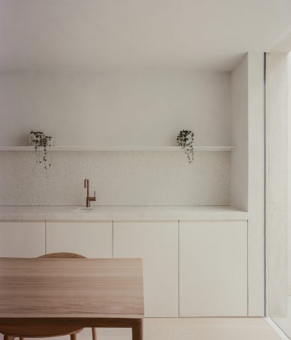 Minimalist white kitchen a white stone worktop, white shelf and wooden dining table and chairs