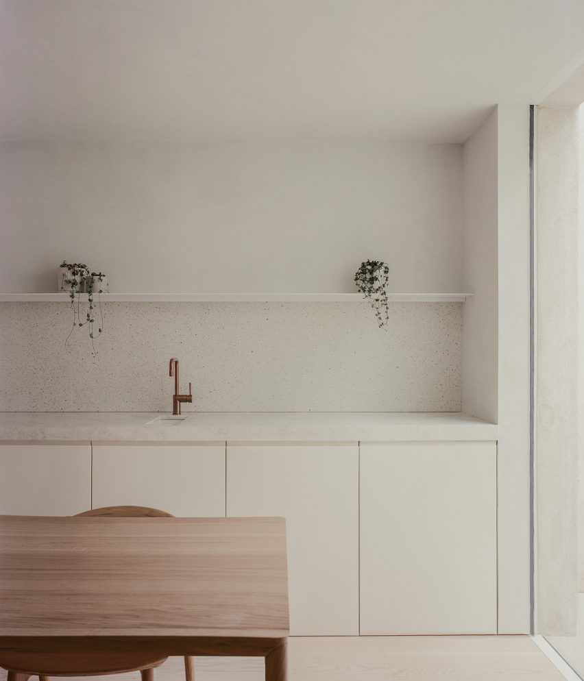 Minimalist white kitchen a white stone worktop, white shelf and wooden dining table and chairs