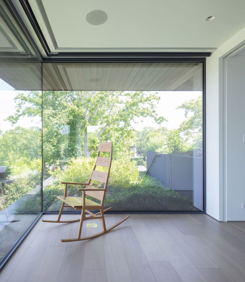 Wooden rocking chair in a room with wooden floors in front of a large corner window overlooking greenery