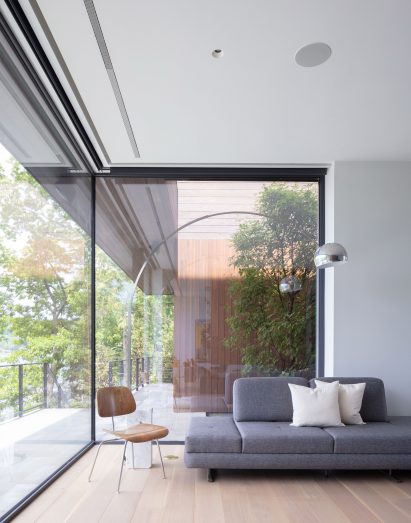 Living space furnished with a sofa, chair and floor lamp in front of a large corner window overlooking a tree