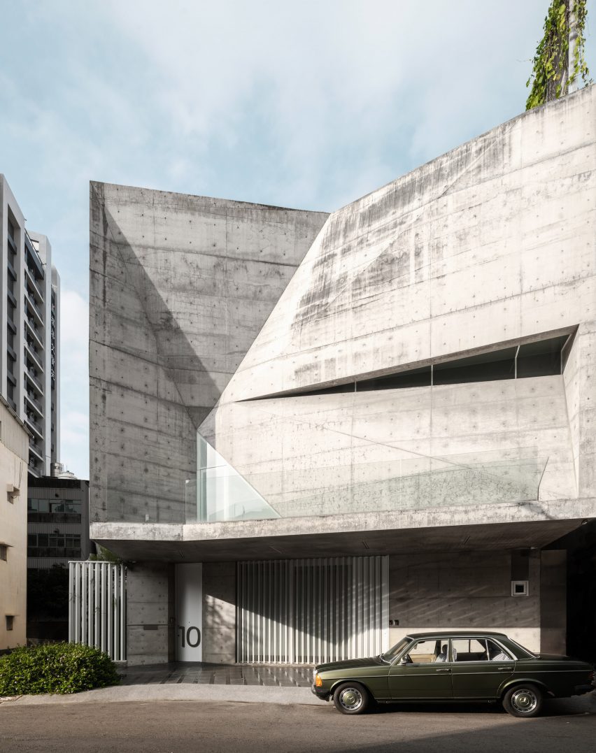 Angular concrete exterior walls of a home with a black car parked in front