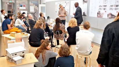 Students presenting architecture work to other students sat on wooden stools