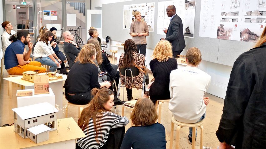 Students presenting architecture work to other students sat on wooden stools