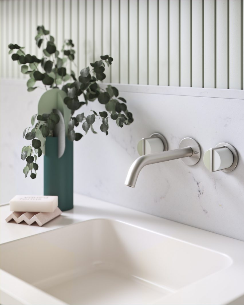 Chrome wall-mounted tap over a cream sink with a vase of leaves