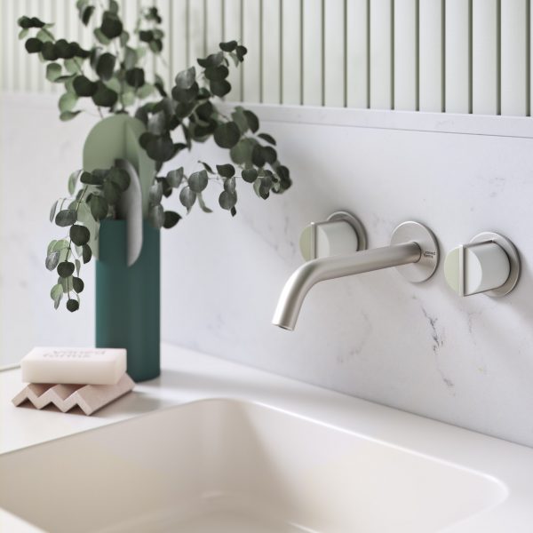 Chrome wall-mounted tap over a cream sink with a vase of leaves