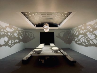 A white rectangular room with a vaulted ceiling and large dining table at the centre