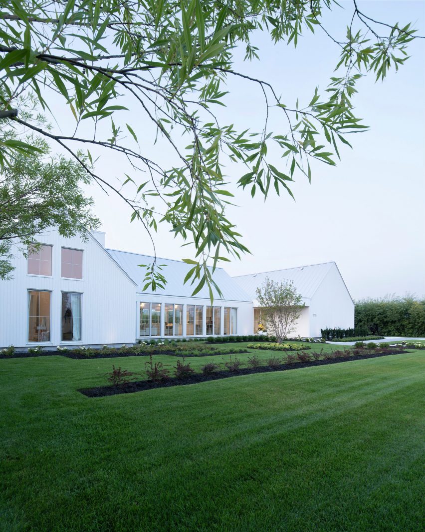 A white U-shaped house with a pitched roof on a green lawn