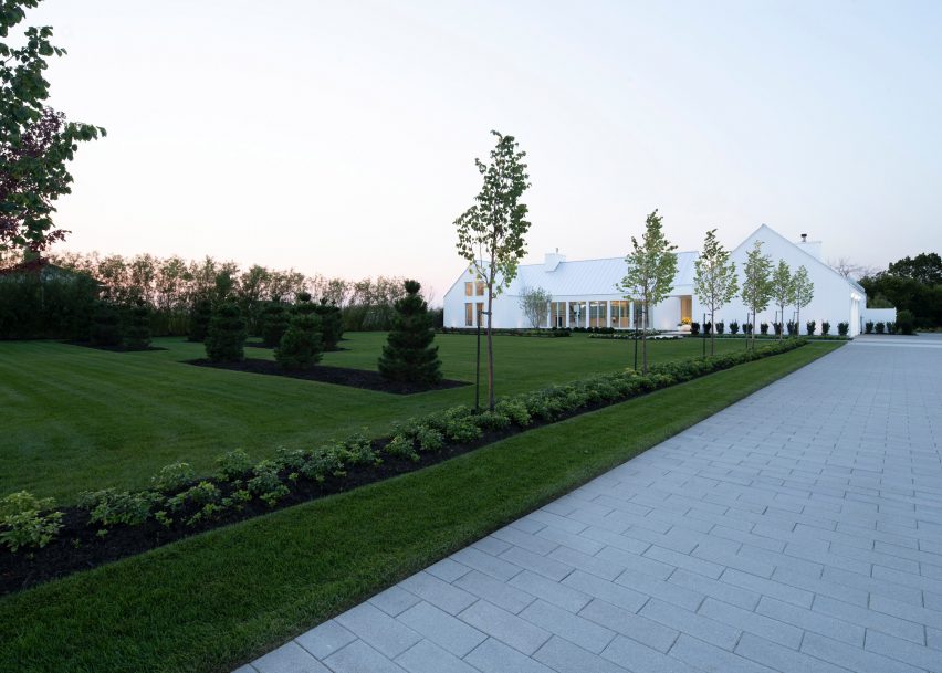 A white U-shaped house with a pitched roof on a green lawn
