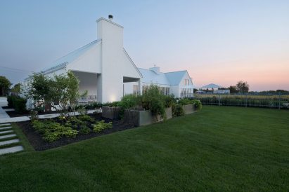 A white U-shaped house with a pitched roof on a green lawn