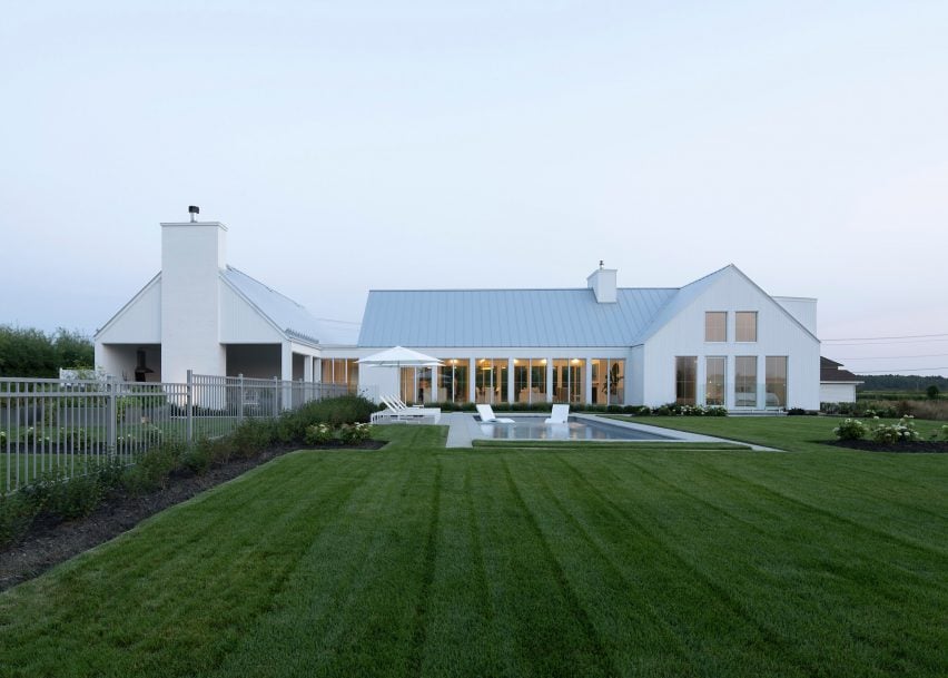 A white U-shaped house with a pitched roof on a green lawn