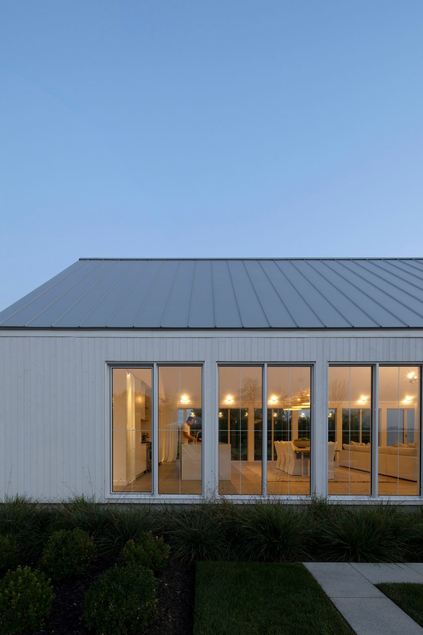 One-storey building with white timber cladding with large windows looking into a dining room