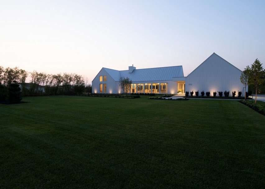 A white U-shaped house with a pitched roof on a green lawn