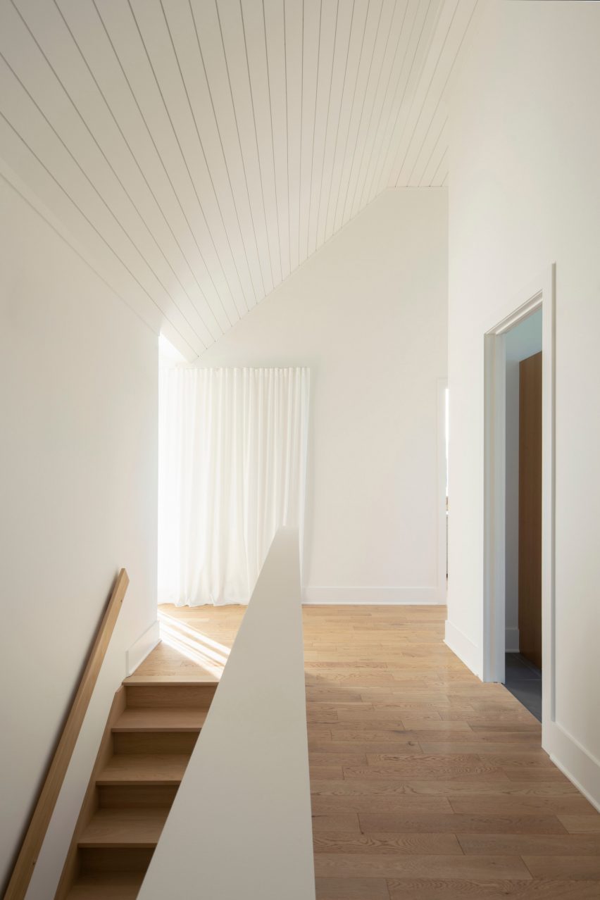 A corridor with white walls and a sloping roof with timber floors and a staircase