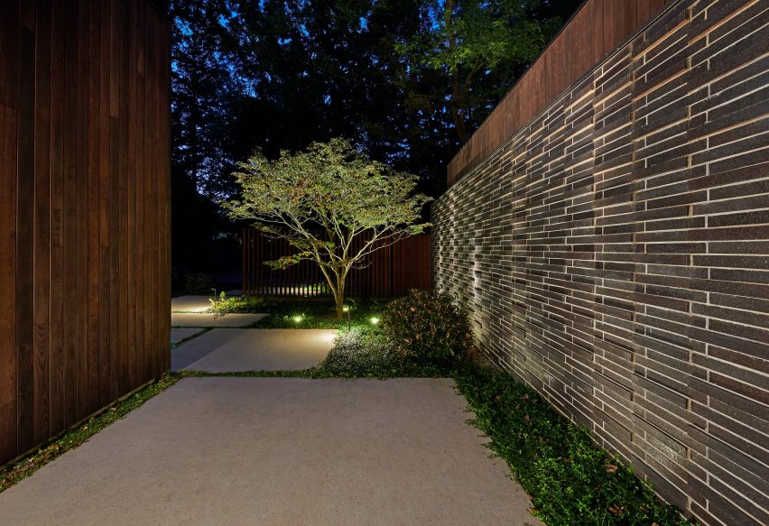 Exterior space with planting, stone paving and a tree lit by outdoor garden lights