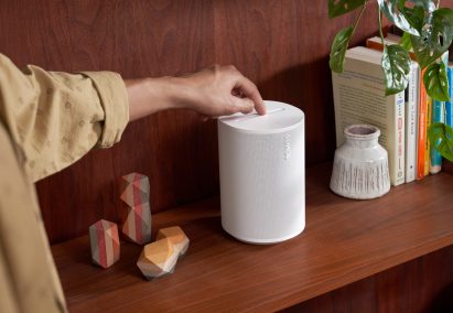 Sonos' Era 100 smart speaker in white on a book shelf