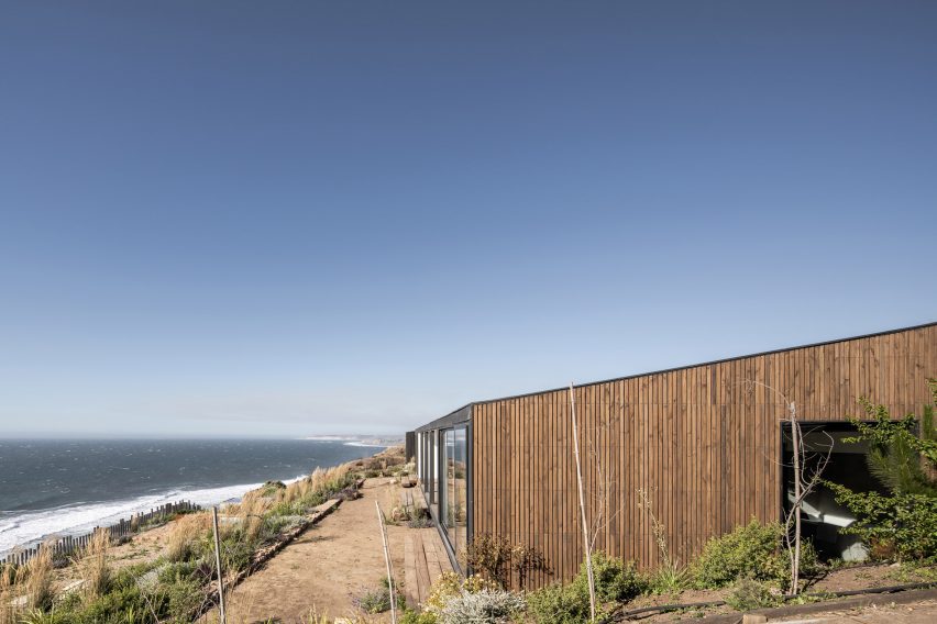 Timber-clad home with a sloping roof on a hillside overlooking the sea