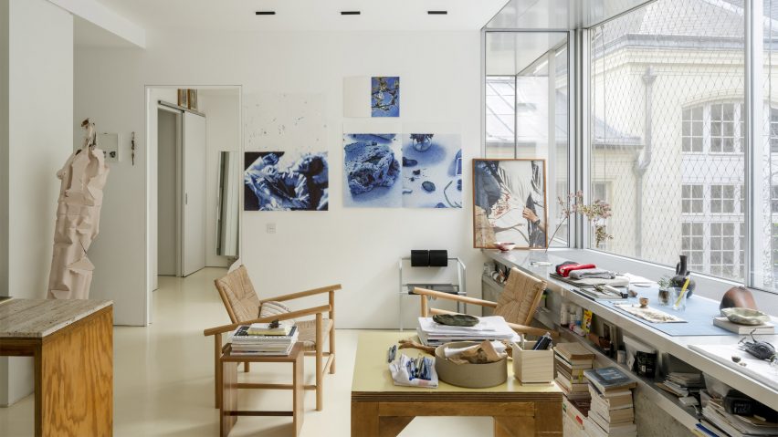 Interior of an office studio with wooden chairs and coffee table, large window and artwork on the walls