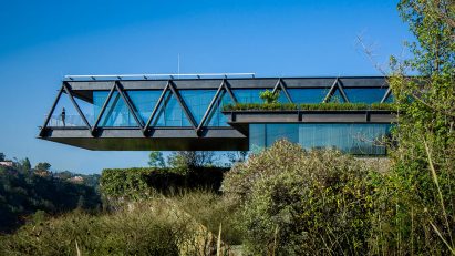 One-storey house with a ddark metal structure cantilevering over bushes