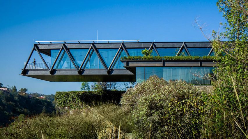 One-storey house with a ddark metal structure cantilevering over bushes