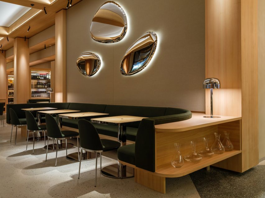 Restautant interior with green upholstered seating, wood tables and chrome wall lights