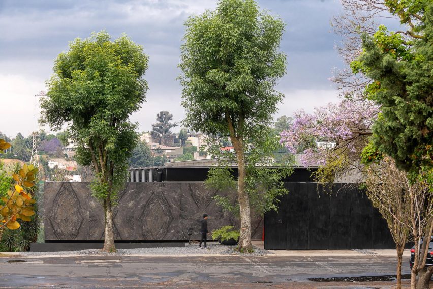 A street with three trees and a low-lying home behind dark grey boundary walls
