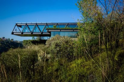 One-storey house with a ddark metal structure cantilevering over bushes
