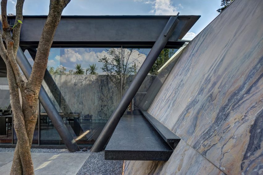 Sloping marble exterior walls with bench seating and a home with a black steel structure
