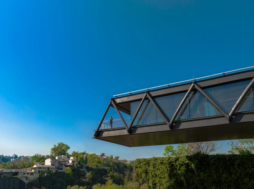 A one-storey black steel structure cantilevering over bushes