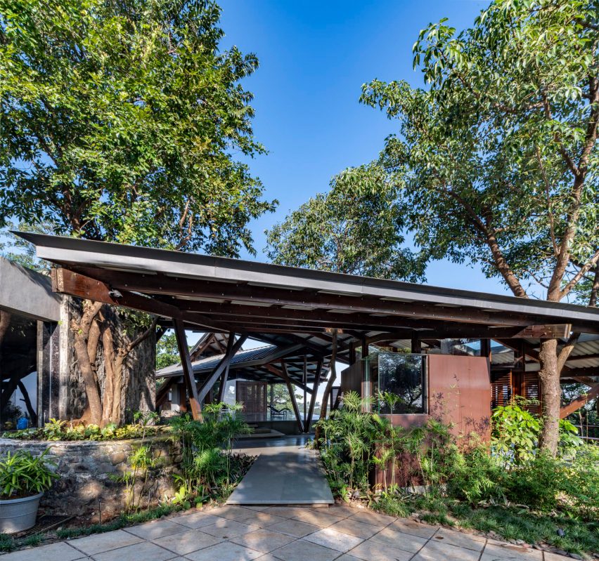 A sloping metal roof covering a terrace in a planted garden