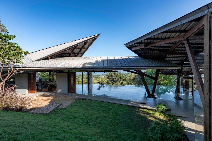 Exterior of a home in India was a grass lawn, terrace with a swimming pool and an angular metal roof