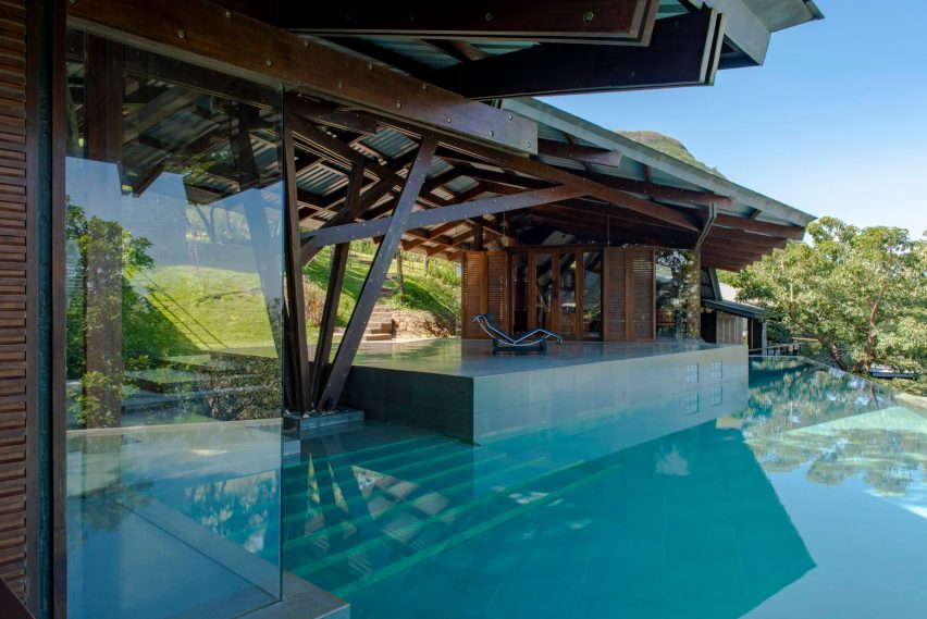 A blue swimming pool with steps leading to a terrace with a timber structure roof overhead