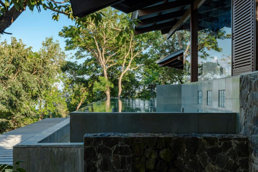 The edge of an infinity swimming pool next to a home overlooking treetops