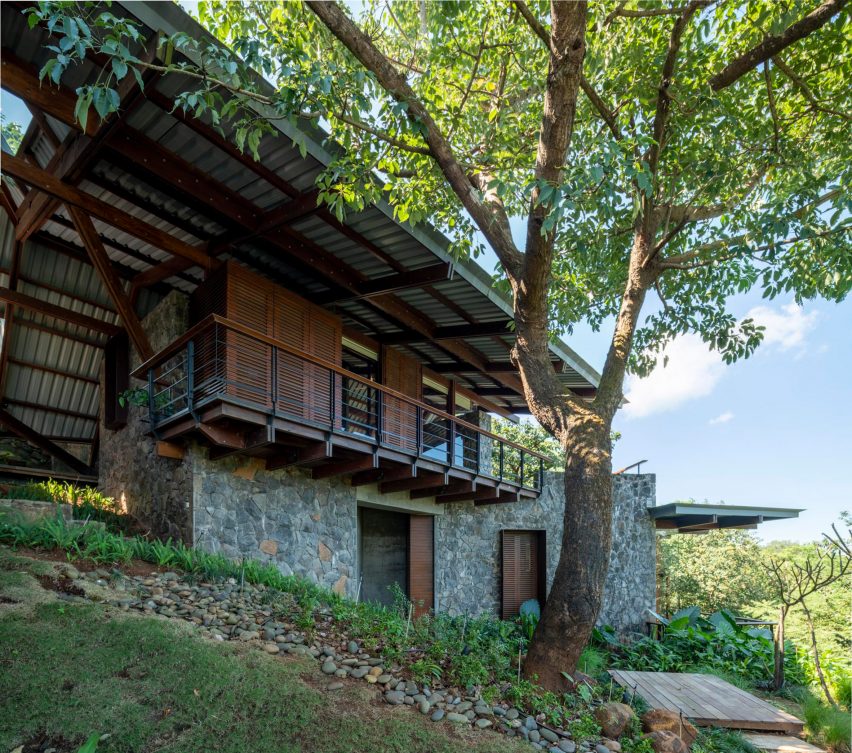 Exterior of a home in India on a grassy slope with stone and timber walls