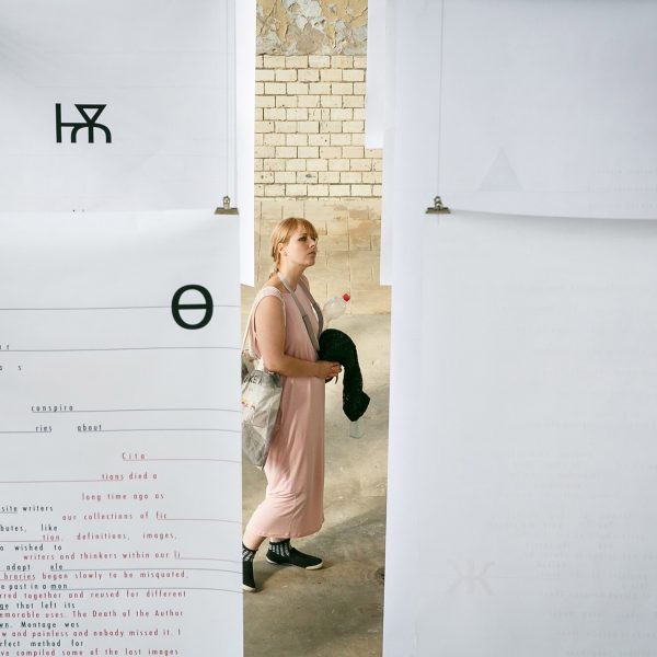 A woman walking around a student exhibit with hanging paper