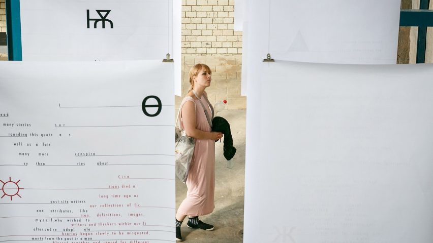 A woman walking around a student exhibit with hanging paper