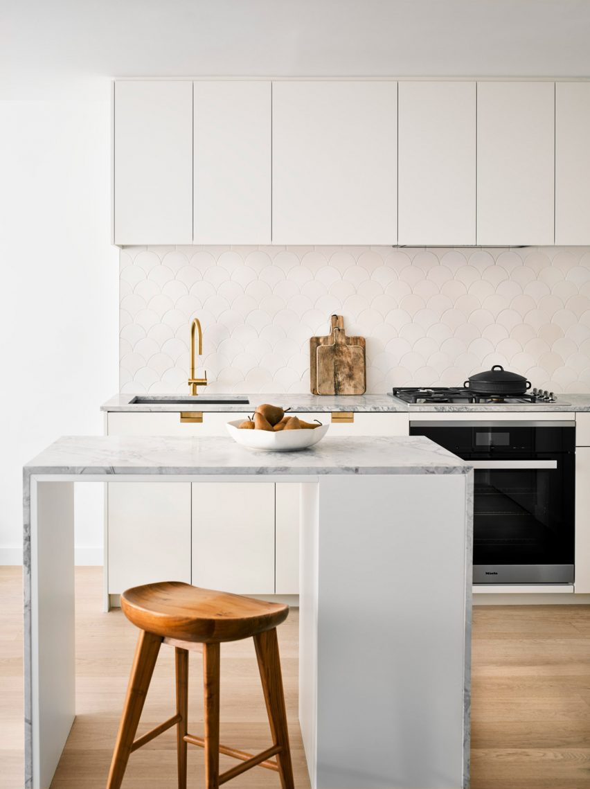 Interior of a kitchen with wooden flooring, white units and a white marble island