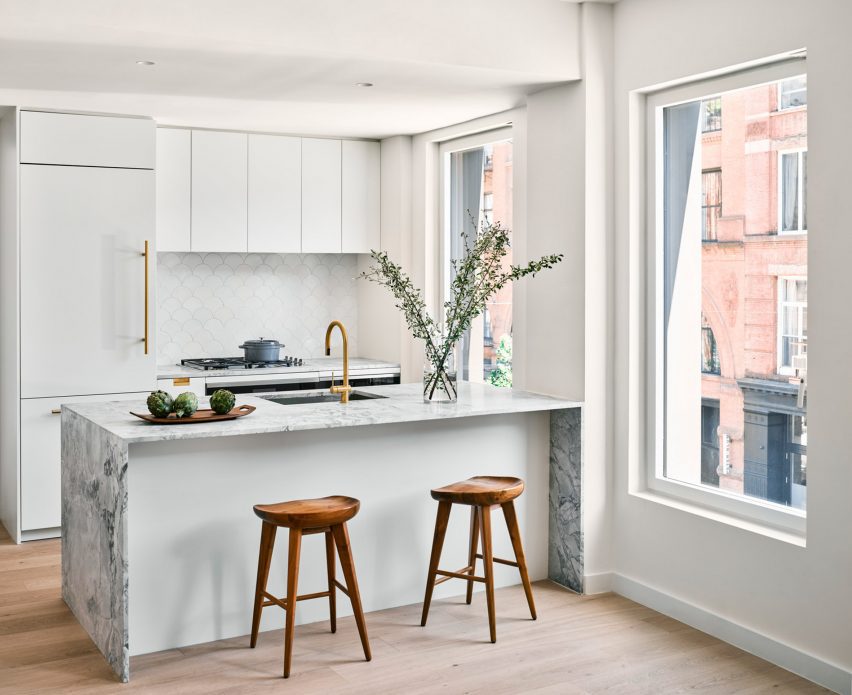 Interior of a kitchen with wood flooring, white kitchen units and a white marble island