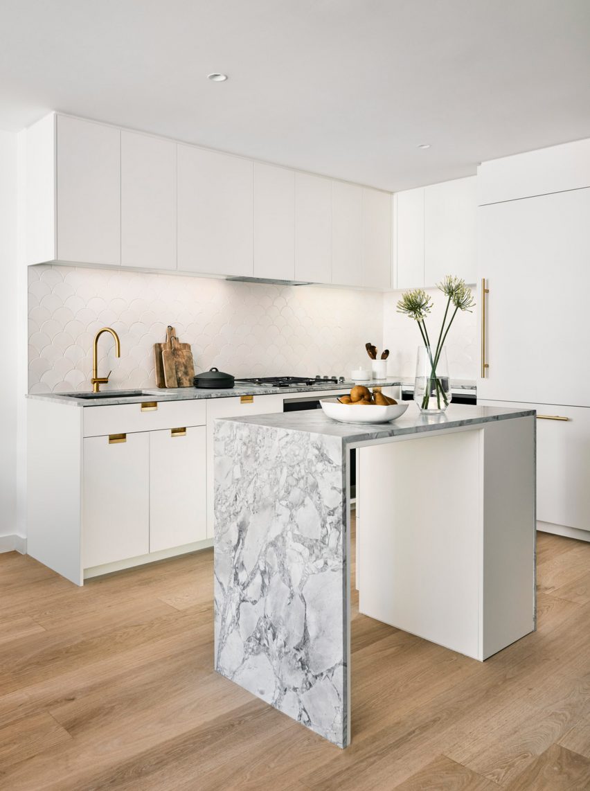 Interior of a kitchen with wooden flooring, white units and a white marble island