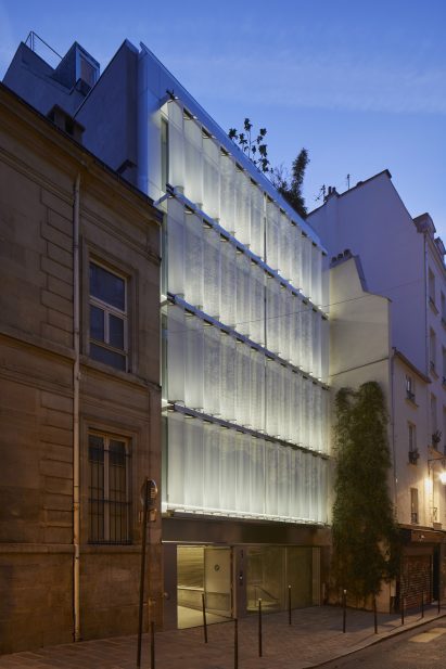 A flat roof building with curved metal moveable curtain wall lit at night