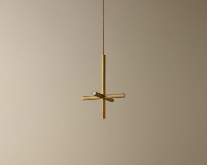 Bronze coloured, cross shaped pendant lamp hanging in front of beige wall