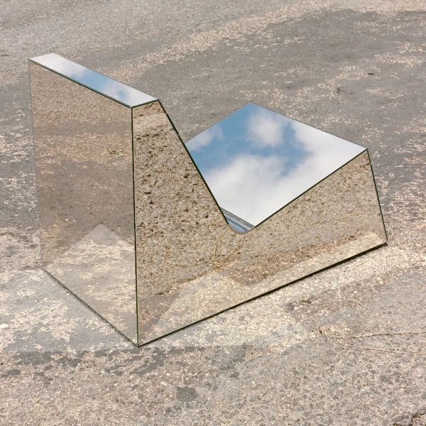 A chair with a mirrored surface on a paved ground